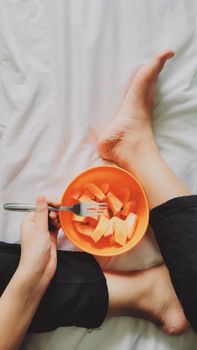Top view of a person enjoying a healthy fruit snack on bed, adding a relaxing vibe to a healthy lifestyle.