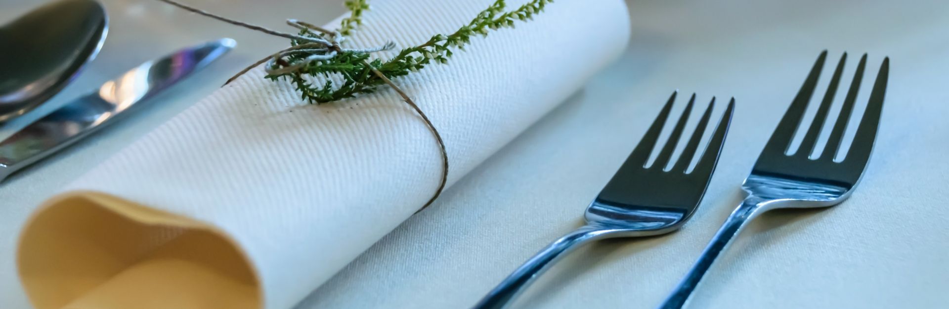 Close-up of a sophisticated table setting featuring a rolled napkin adorned with a sprig and polishe