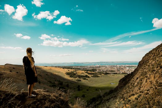 A woman enjoys the breathtaking view over Edinburgh from a hillside during the day.