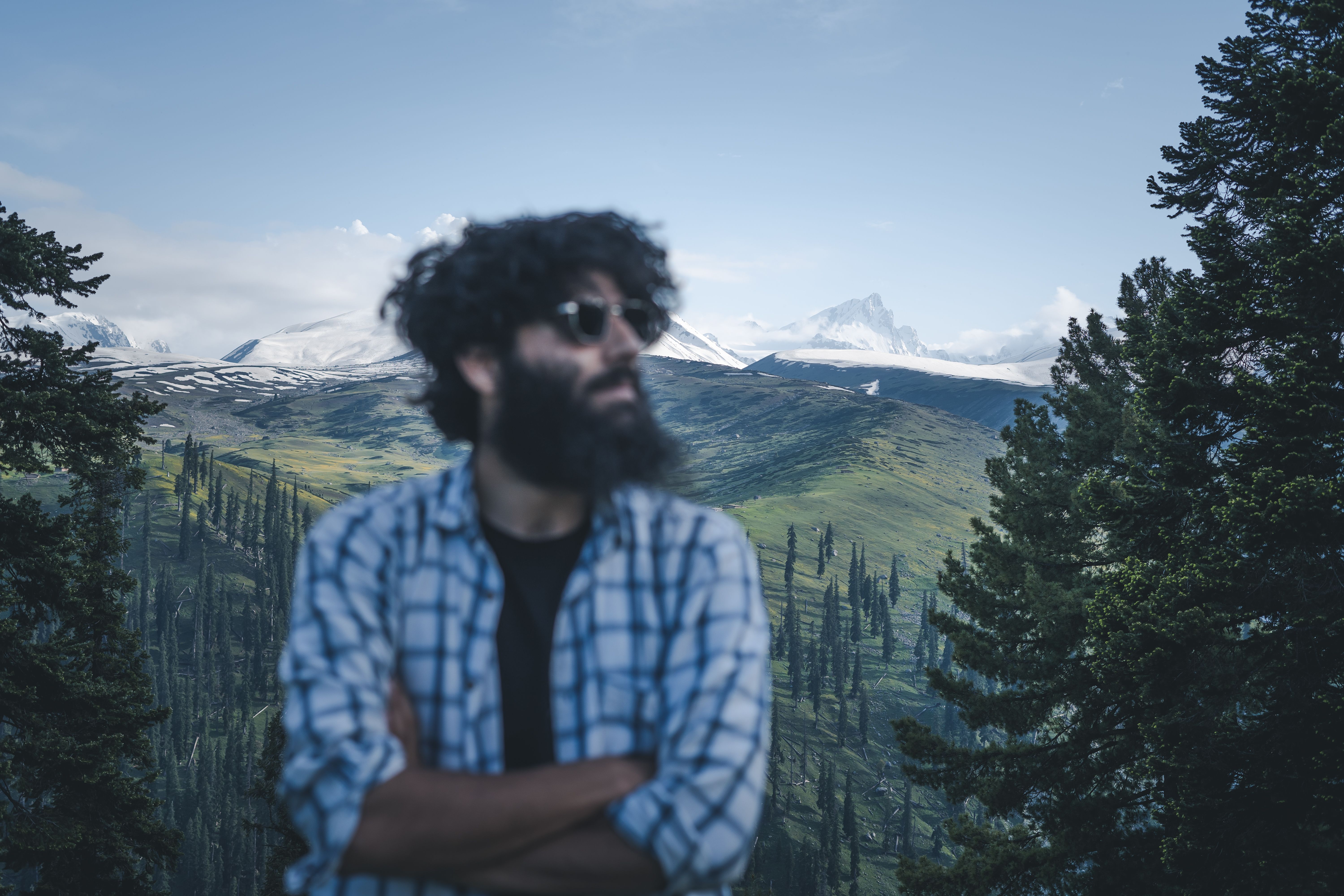 A bearded man stands with arms crossed, enjoying the scenic view of Srinagar's lush landscape.