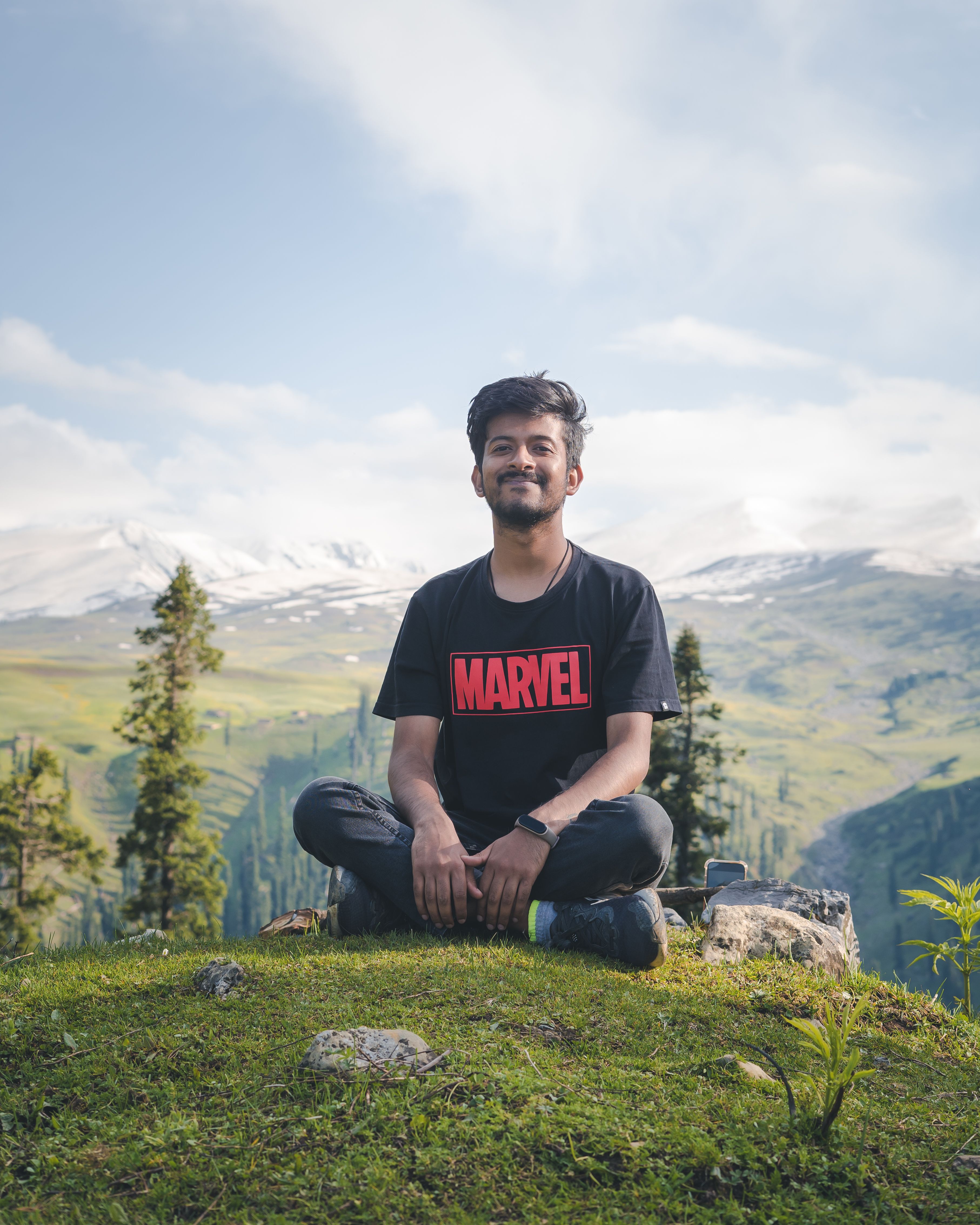 Young man smiling while sitting on a grassy hill in Srinagar's picturesque landscape