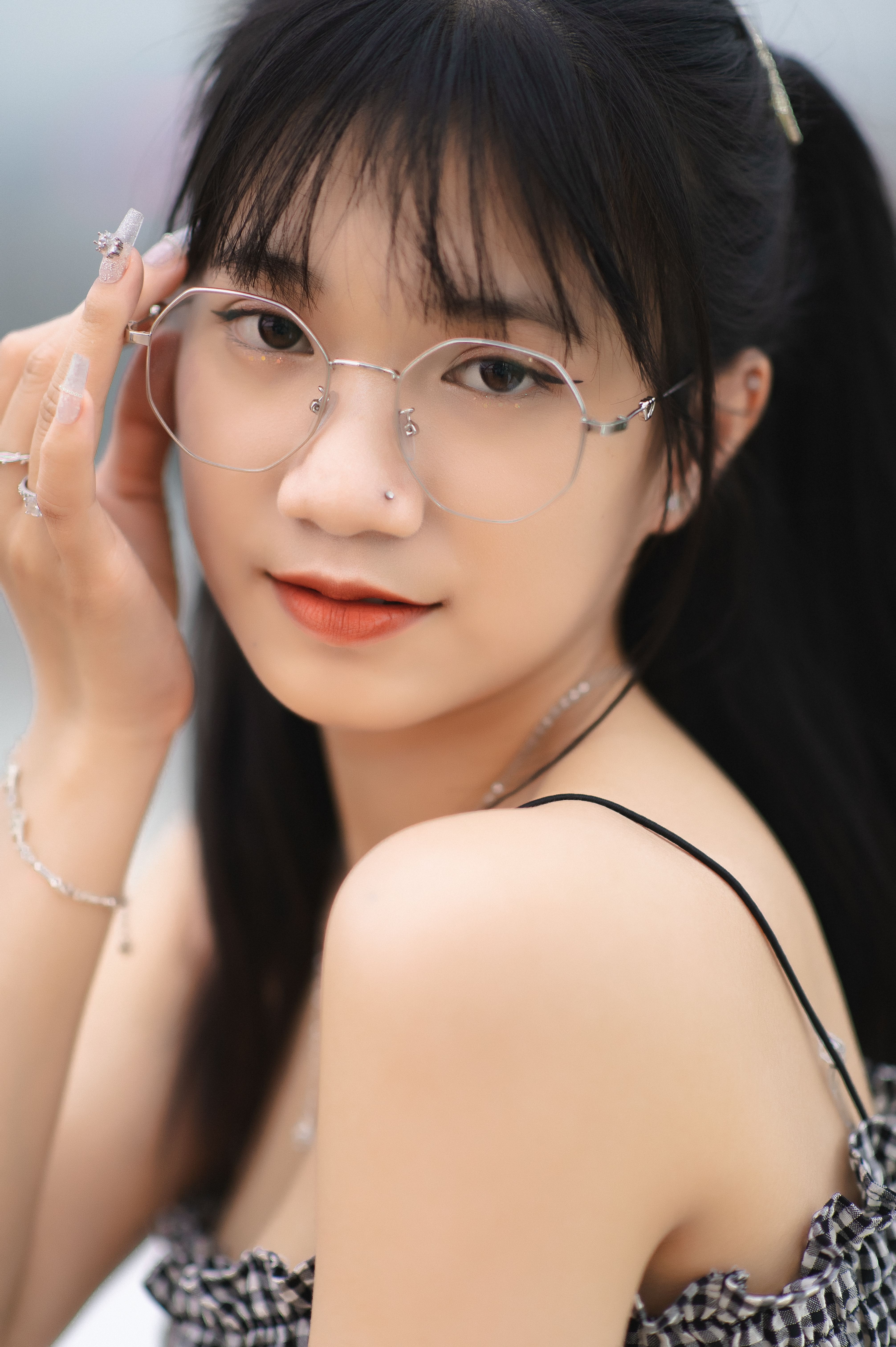 Portrait of a young Asian woman with eyeglasses and bangs, posing gracefully outdoors.