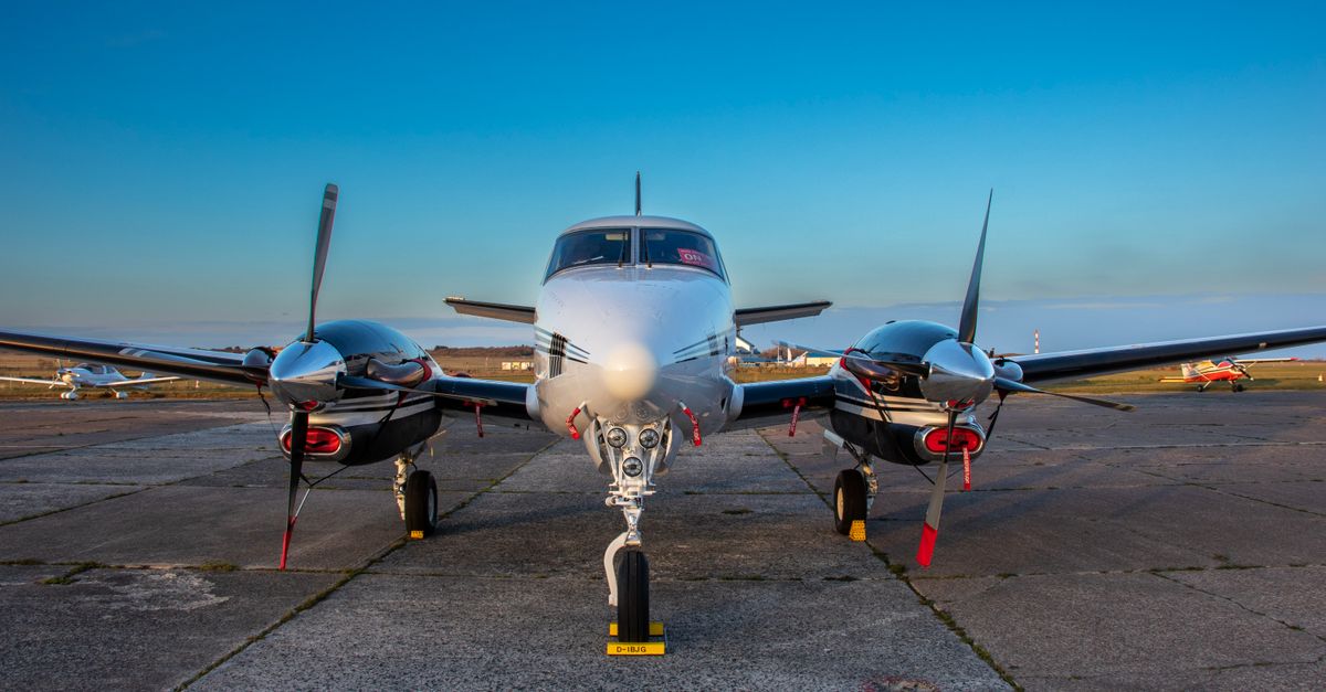 A front view of a twin-engine aircraft on tarmac under clear blue skies.