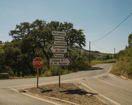 A rural road intersection with directional signs under a clear blue sky in Portugal.