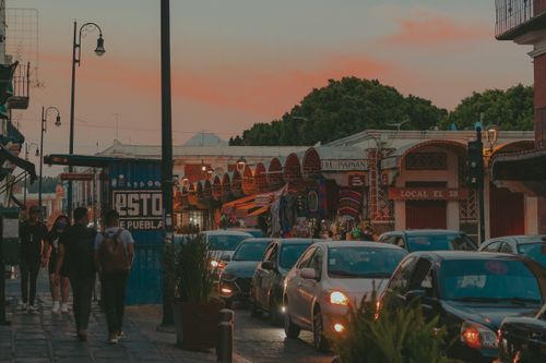 Free Vibrant street scene at dusk in Mexico, showcasing bustling traffic and city life with colorful shops and pedestrians. Stock Photo