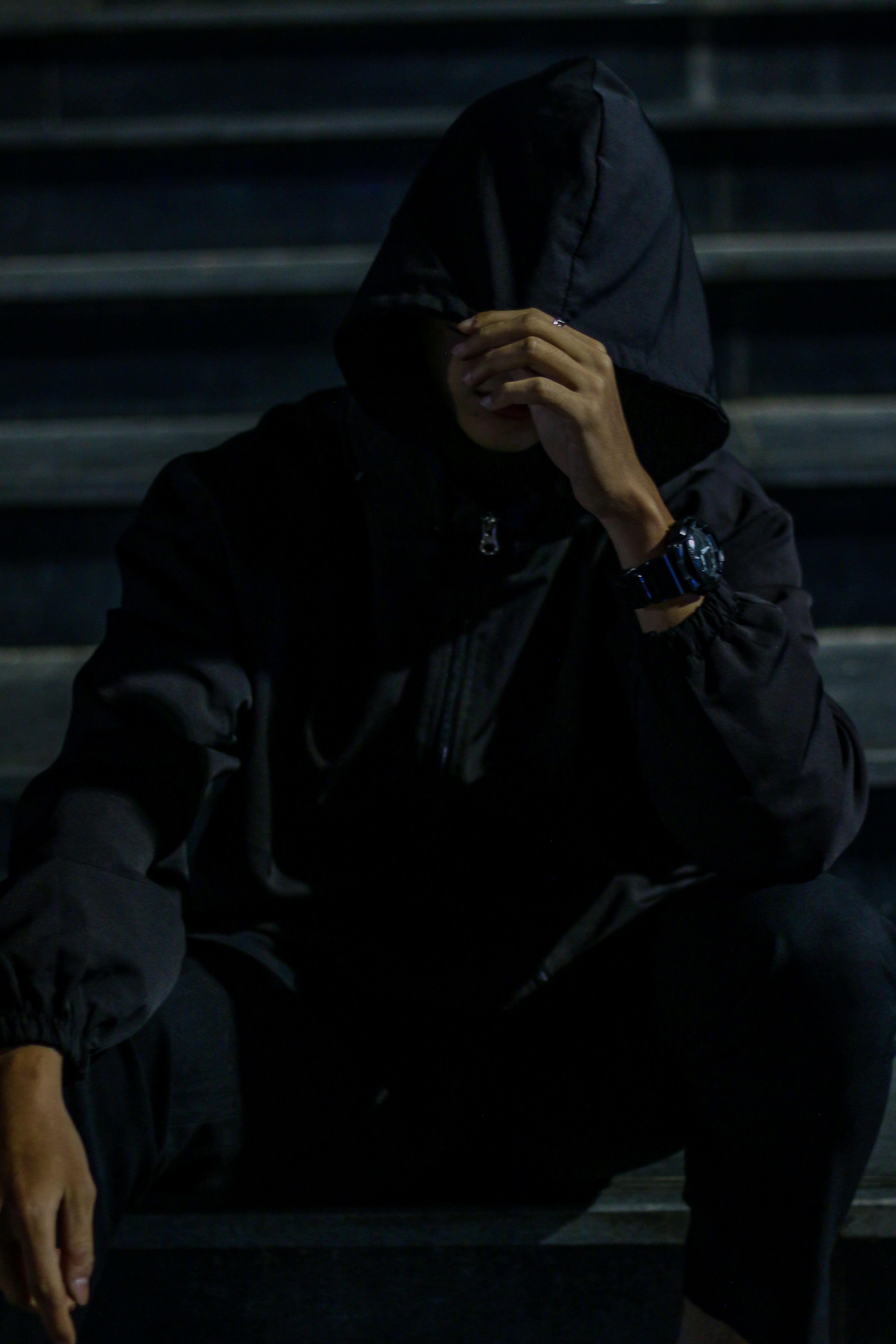 A man in a dark hoodie sitting on steps at night, creating a mysterious urban vibe.