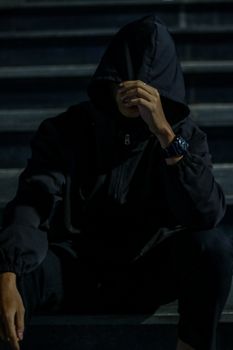 A man in a dark hoodie sitting on steps at night, creating a mysterious urban vibe.