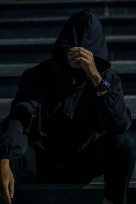A man in a dark hoodie sitting on steps at night, creating a mysterious urban vibe.