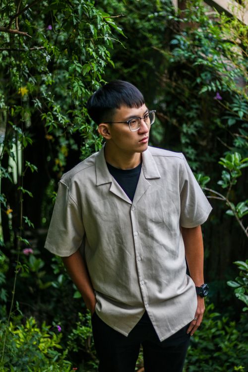 Free Portrait of a young man with eyeglasses posing outdoors against a lush green backdrop. Stock Photo
