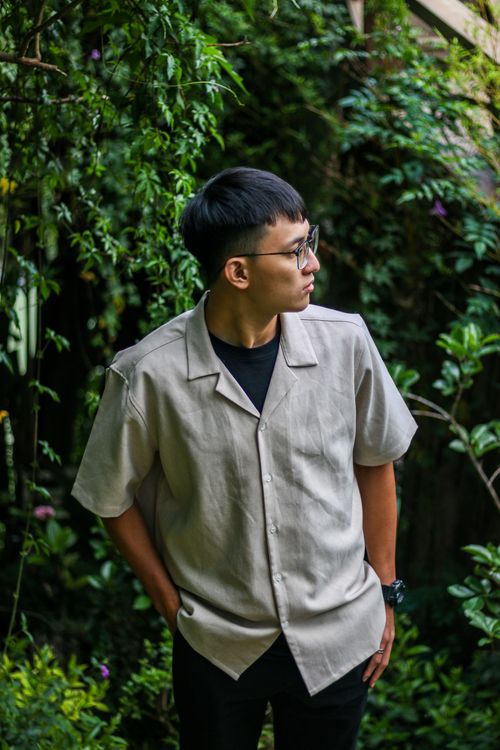 Free Man with eyeglasses in a casual summer shirt standing outdoors surrounded by greenery. Stock Photo