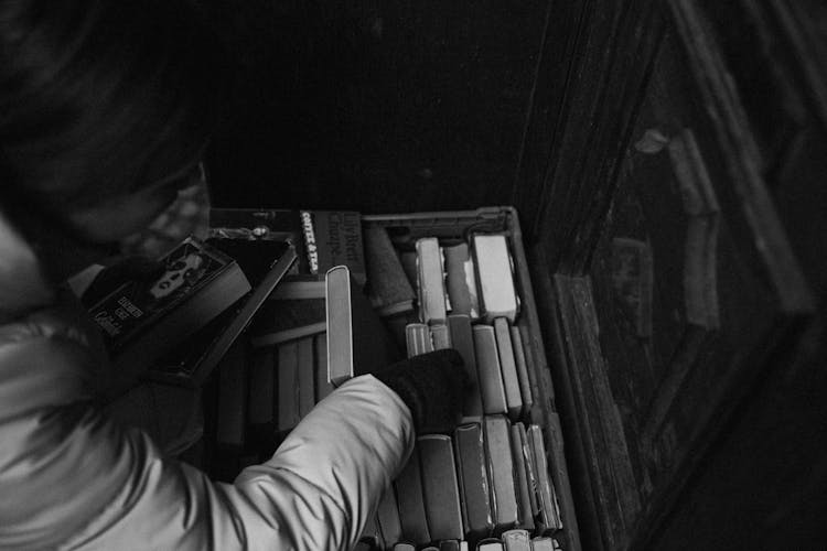 A Woman Looking Through Old Books In A Box