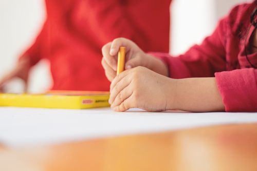 Free A child focuses on drawing with a yellow pencil in a classroom setting. Stock Photo