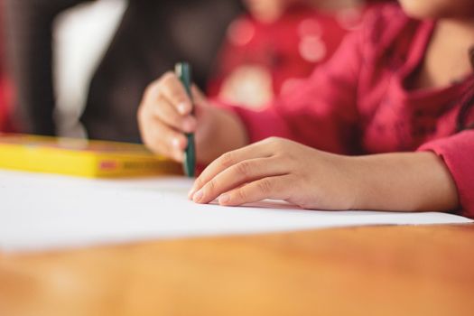 Child drawing with crayons on paper, focusing on creative play indoors.