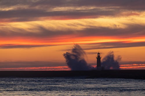 View of Waves Crashing near a Lighthouse under a Dramatic Sunset Sky 