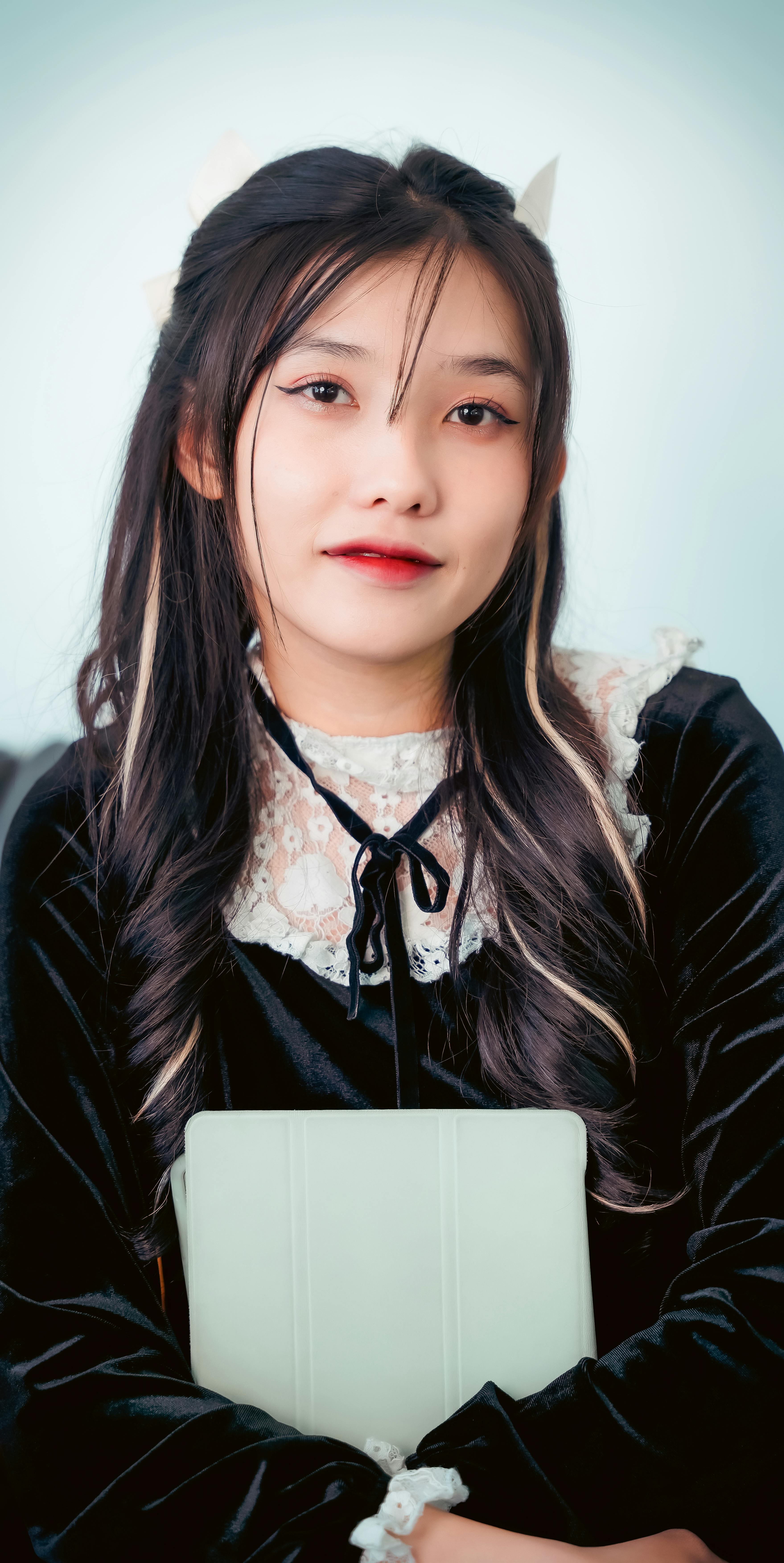 Stylish portrait of an Asian woman in a velvet dress holding a tablet against a white background.