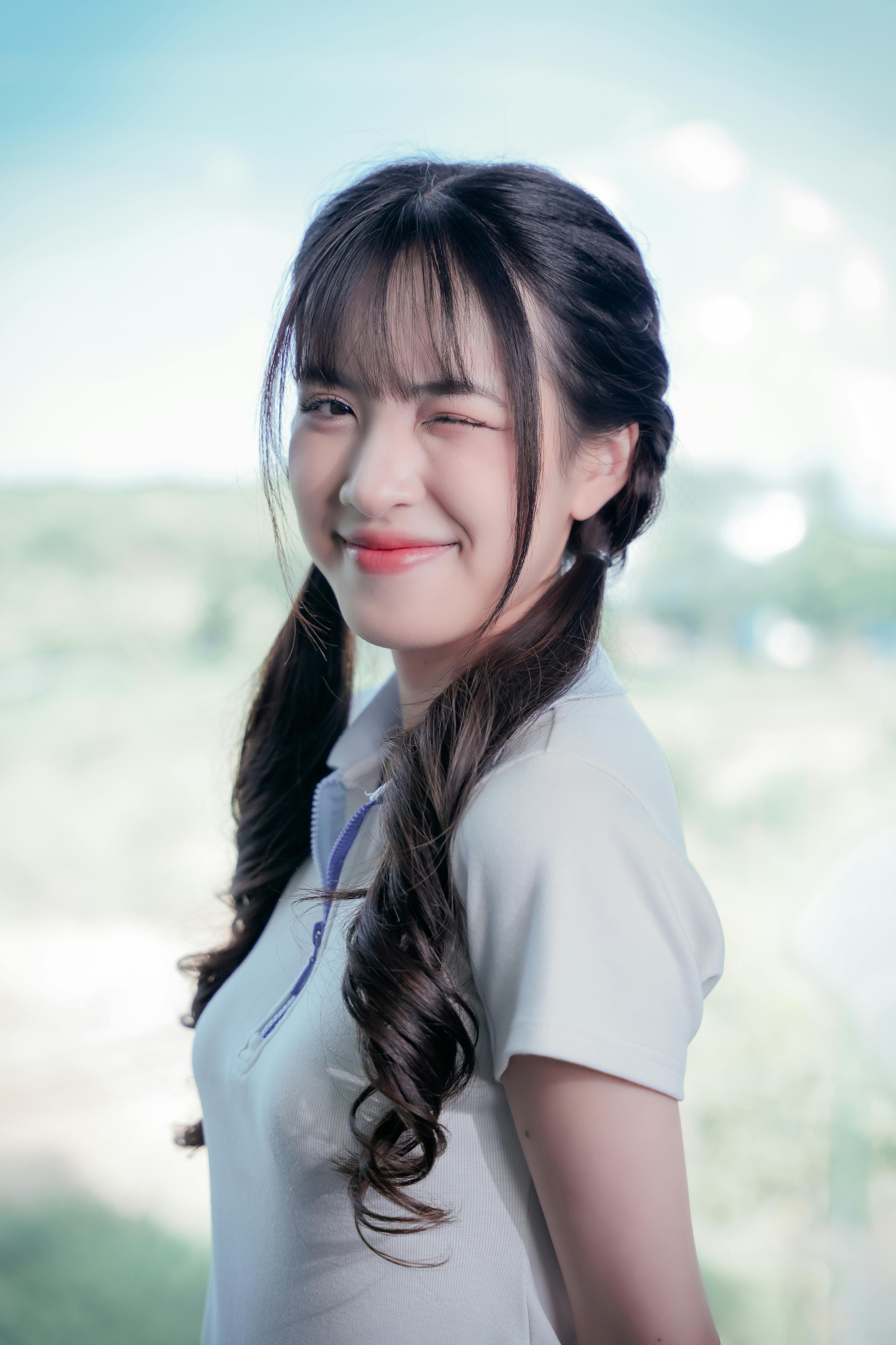 Smiling young woman in white polo shirt posing outdoors with braided hair and winking