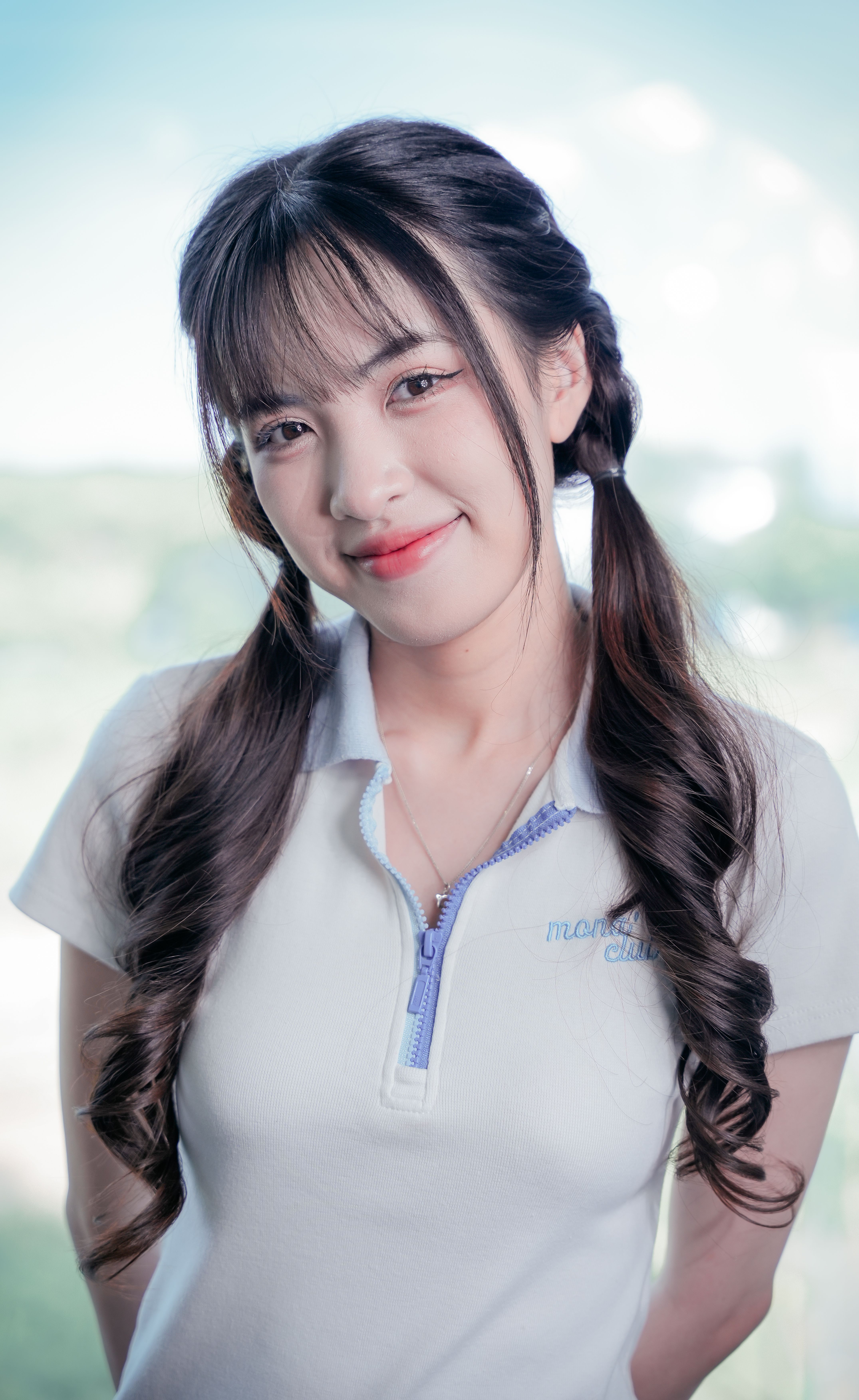 Portrait of an Asian woman with braided hair in a casual white polo shirt, smiling outdoors.