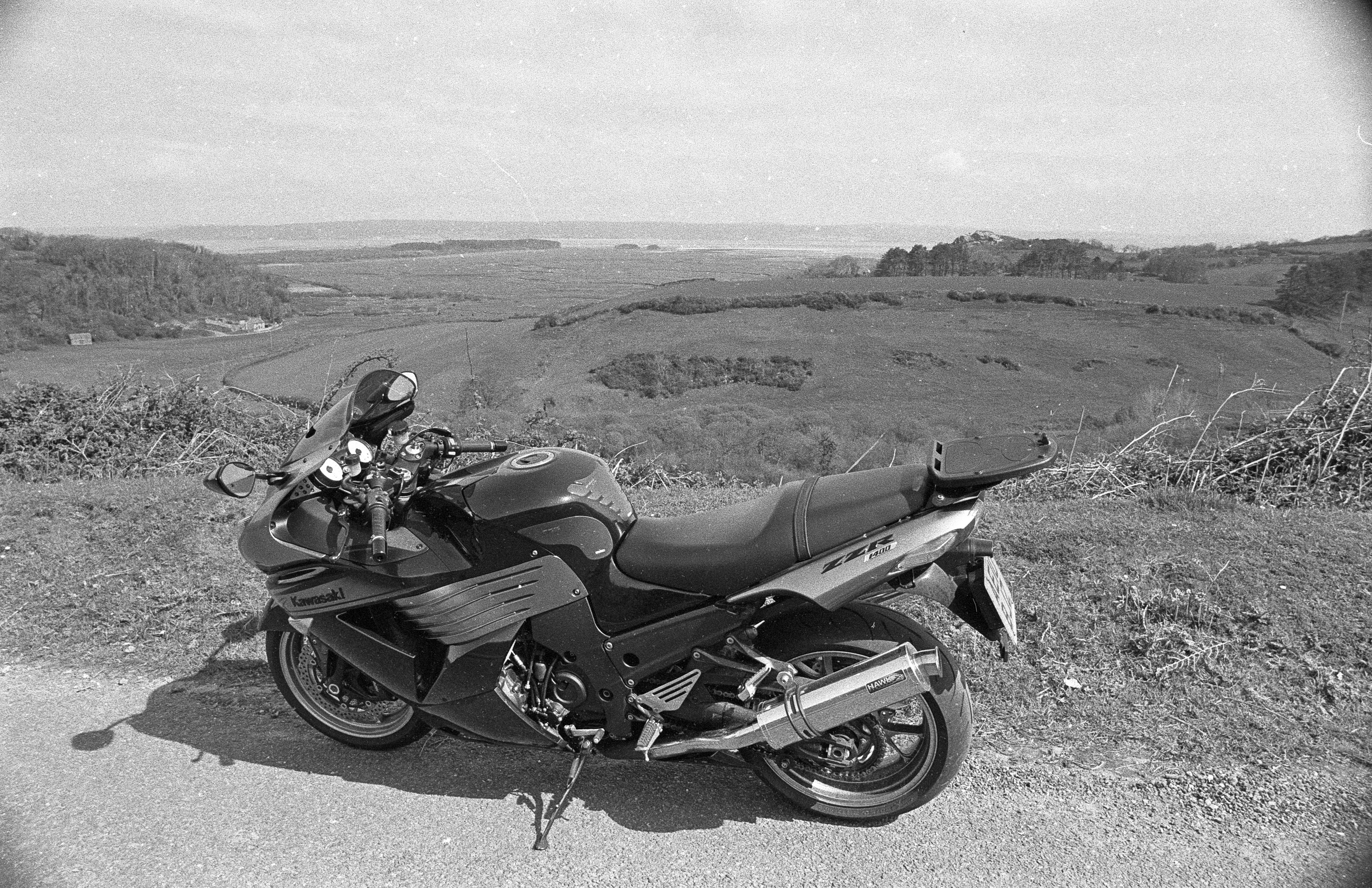 A black Kawasaki motorcycle parked on a rural road, overlooking a scenic valley landscape.