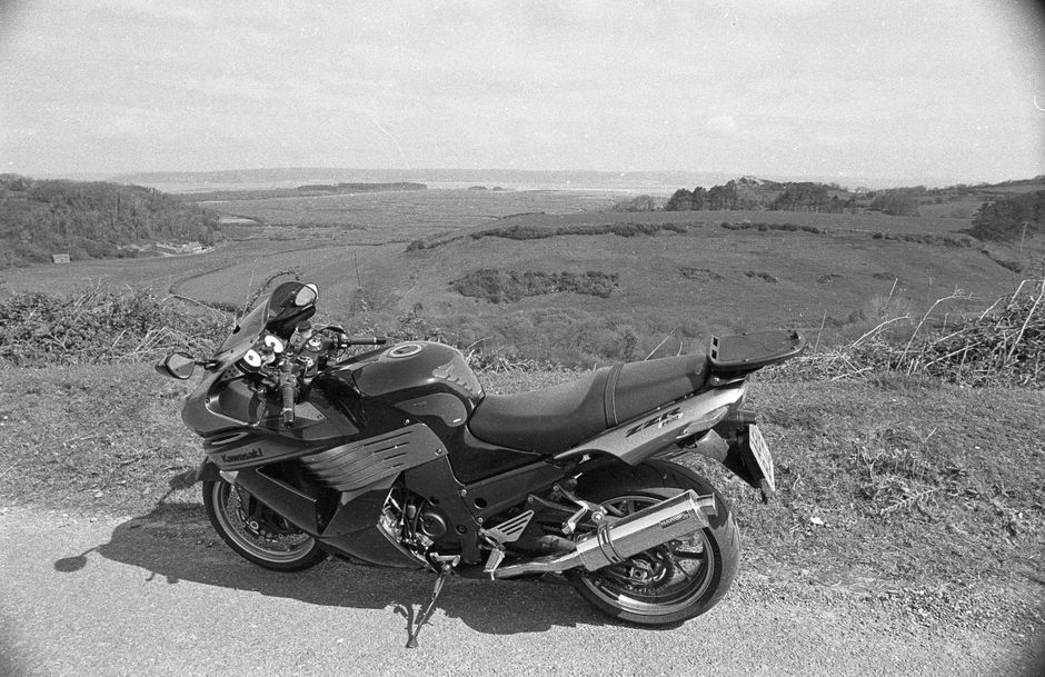 A black Kawasaki motorcycle parked on a rural road, overlooking a scenic valley landscape.