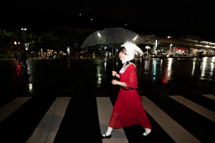 Smiling Woman In Red Dress Walking With Transparent Umbrella At Night