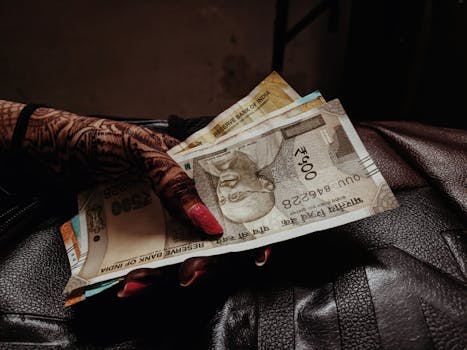 A hand with henna and painted nails holding multiple Indian rupee banknotes.