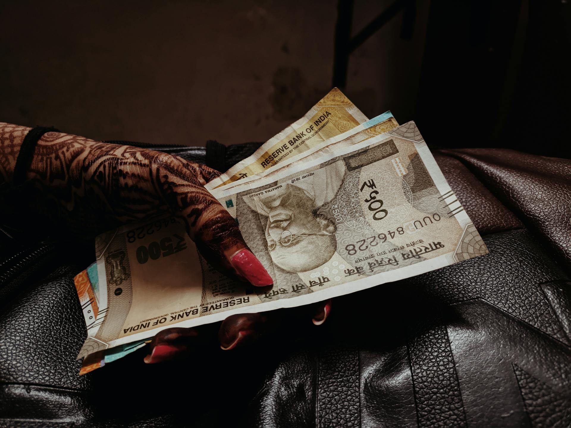 A hand with henna and painted nails holding multiple Indian rupee banknotes.