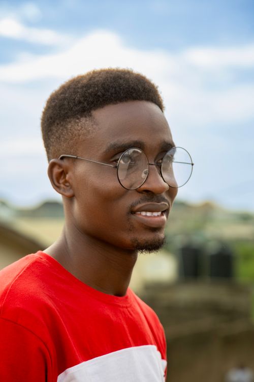 Free A cheerful young man with glasses, smiling in a bright outdoor setting. Stock Photo