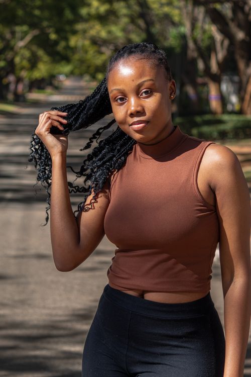 Free Fashionable woman in a brown top with braided hair posing outdoors on a city street. Stock Photo