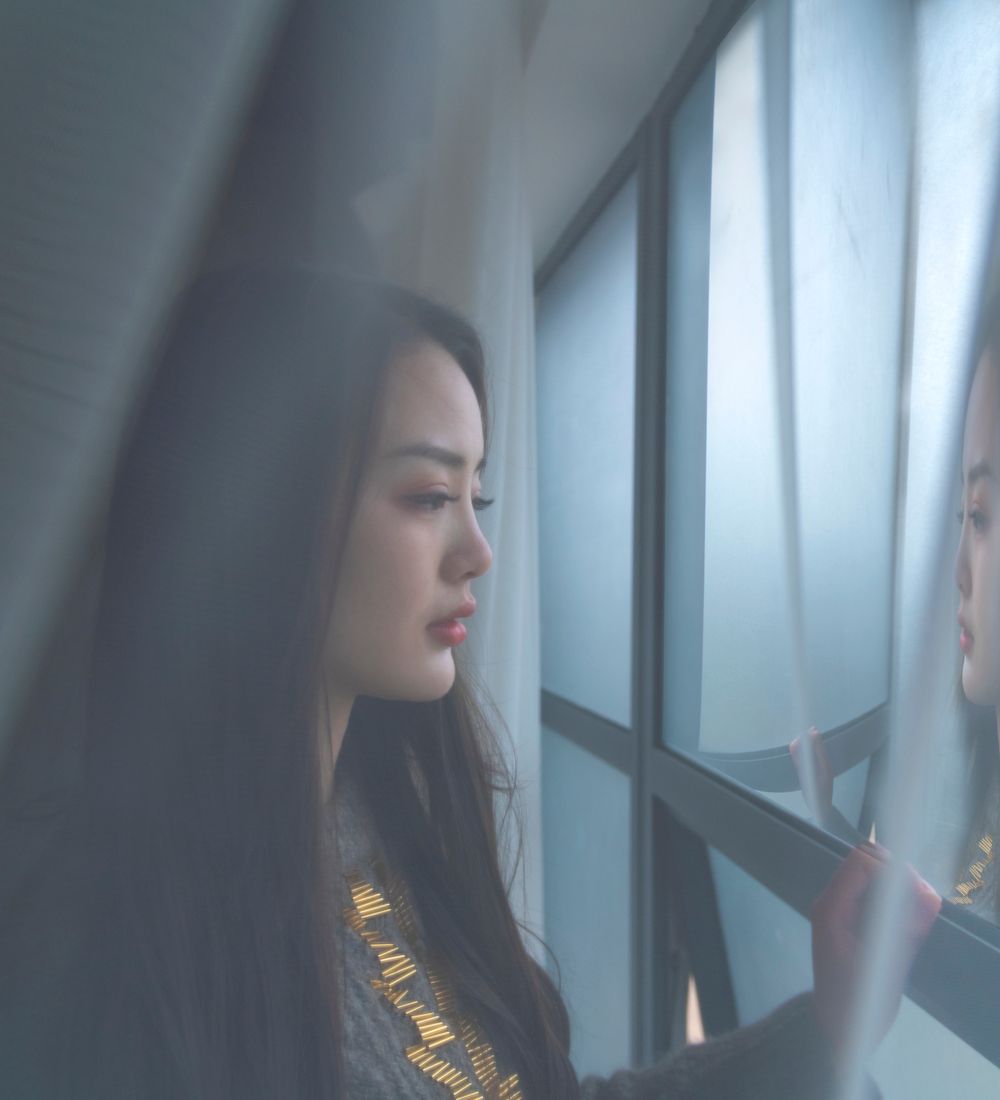 A person standing quietly by a window, taking time to themselves