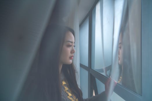 柔和的灯光下，一名女子站在窗前沉思