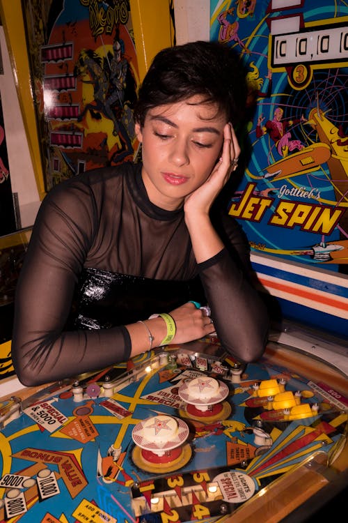 Young Woman Sitting next to a Pinball Machine in an Arcade 
