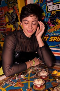 A woman plays a vintage pinball game in a colorful arcade setting, symbolizing fun and nostalgia.