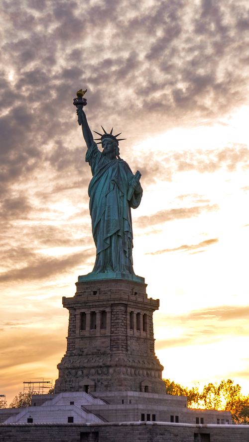 Free Stunning sunset view of the Statue of Liberty against a vibrant sky in New York City. Stock Photo