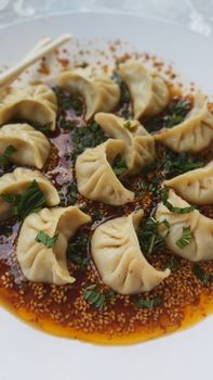 A mouthwatering plated dish of dumplings in a spicy sesame sauce garnished with herbs.