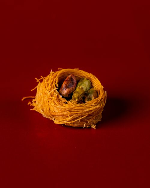 Free Close-up of traditional Turkish baklava nest with pistachios on a vibrant red background. Stock Photo