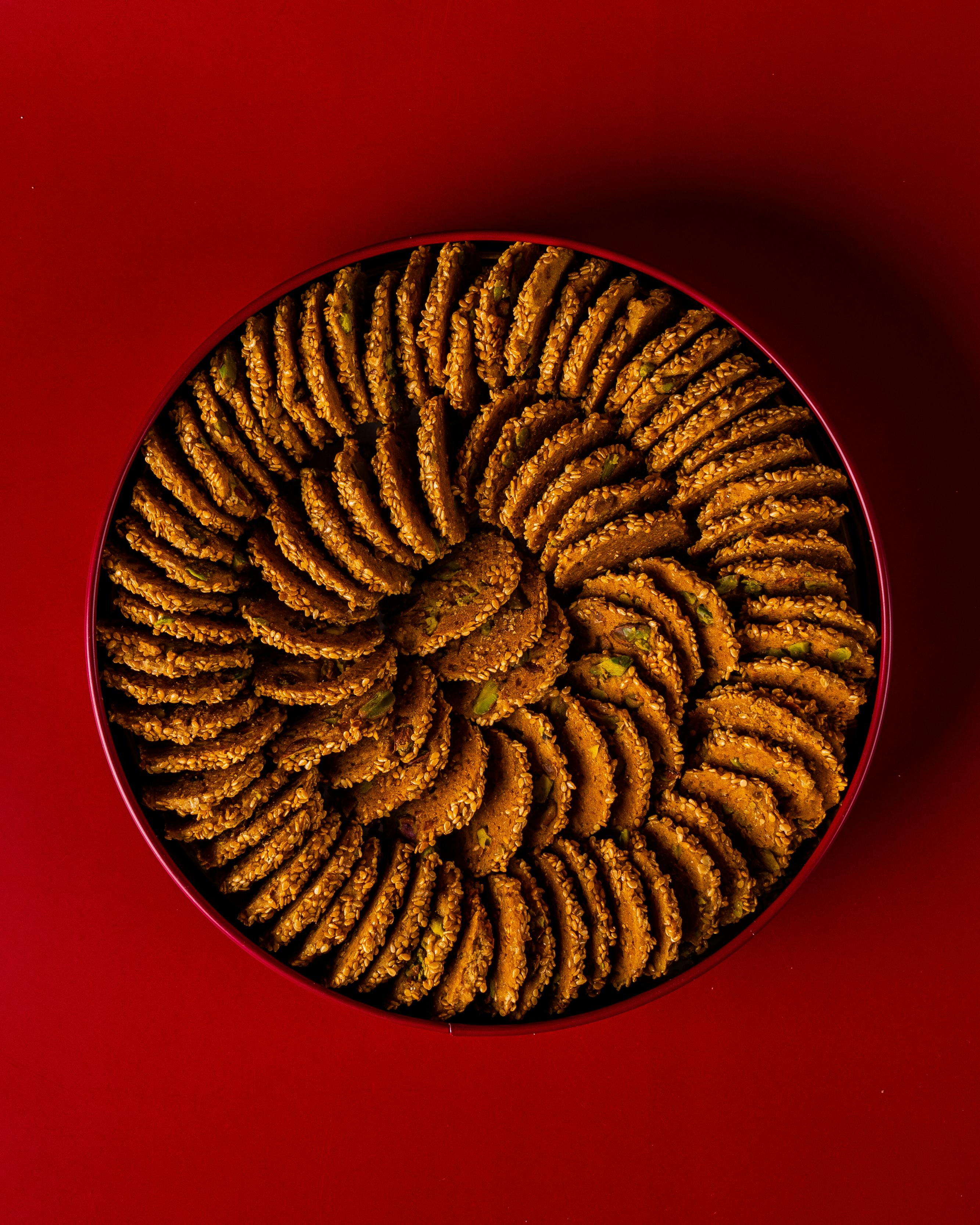 Delicious sweet cookies arranged neatly in a round tin on a vibrant red background, perfect for festive treats.