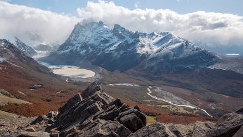 View of Snowy Mountain Peaks and a Valley with Trees in Autumnal Colors 