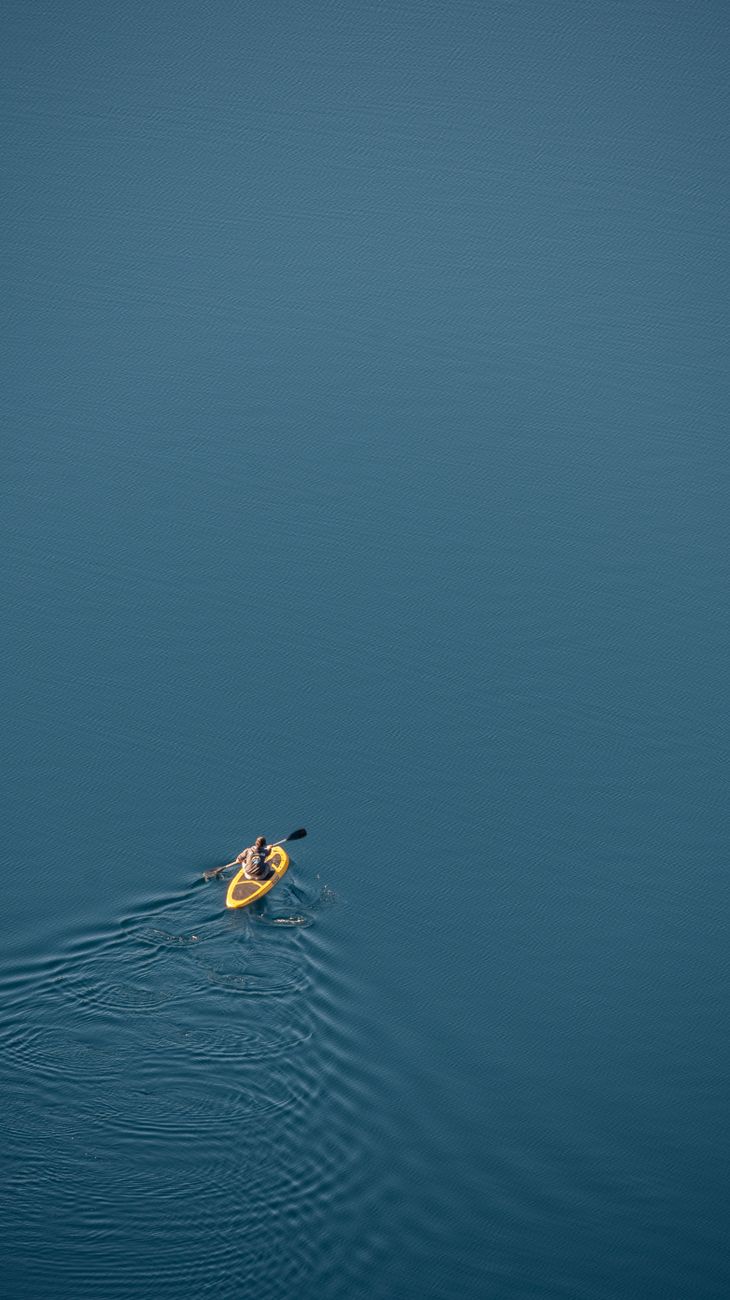Aerial view of a lone kayaker paddling on a tranquil, expansive blue lake in Patagonia.