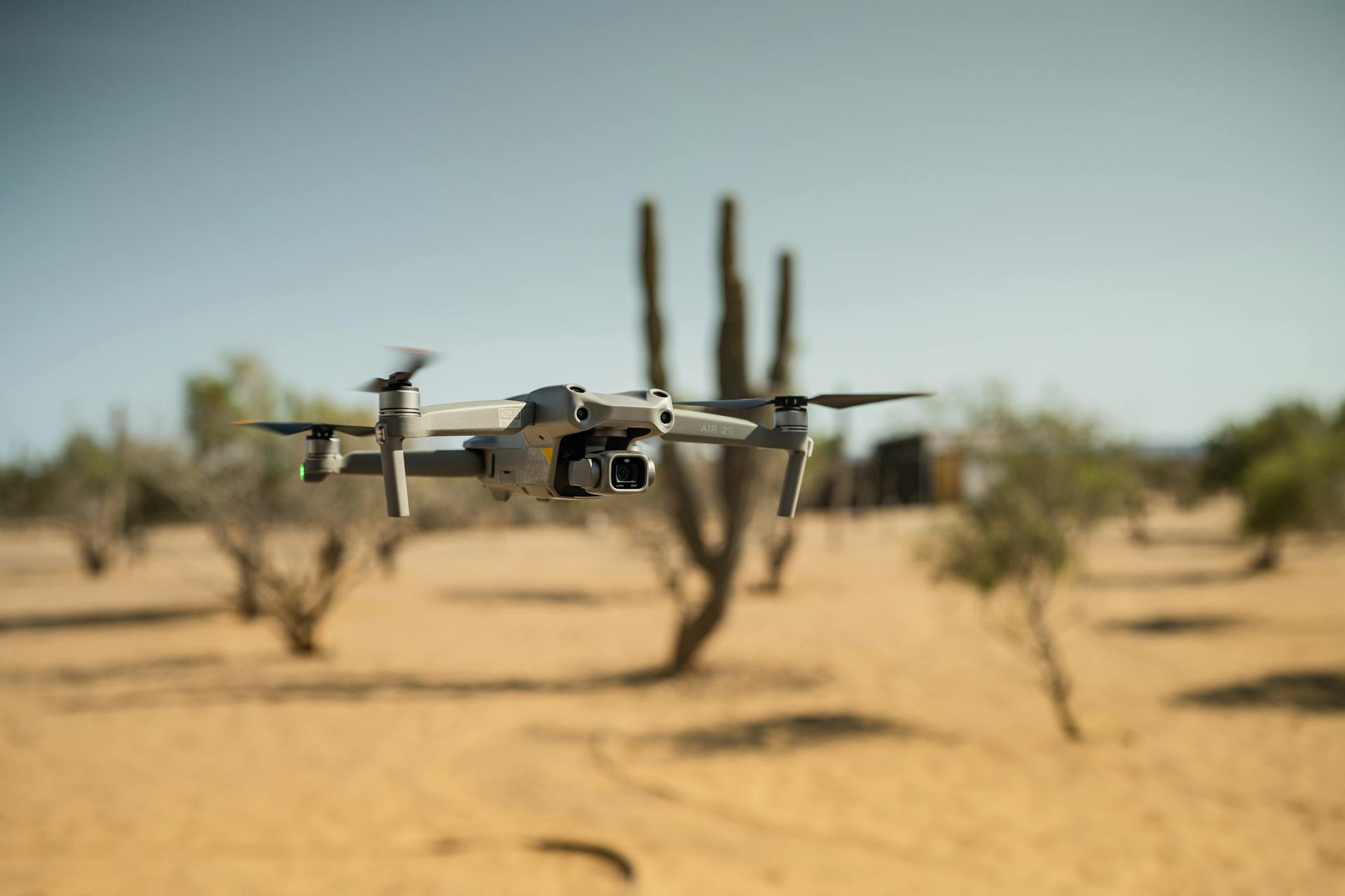 Close-up of a drone with propellers flying over a desert landscape, showcasing technology.