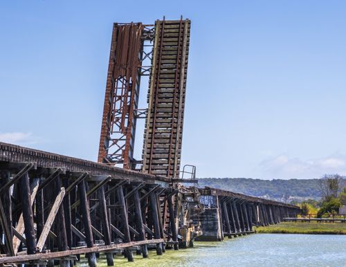 Free Industrial lifting bridge with rail tracks over a serene river under a clear blue sky. Stock Photo
