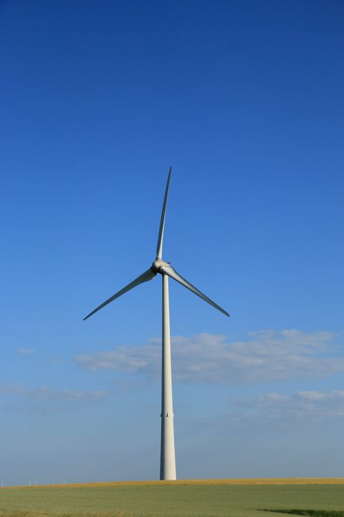 Free A solitary wind turbine stands tall under a vibrant blue sky in a peaceful field. Stock Photo