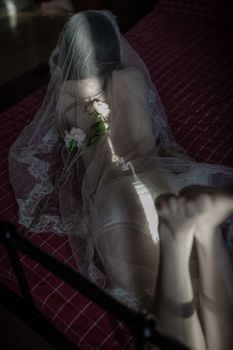A woman lies on a bed, draped in lace, holding flowers, exuding sensuality and elegance.
