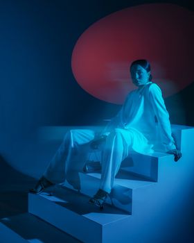 Fashion model in white attire posing on stairs with blue lighting.