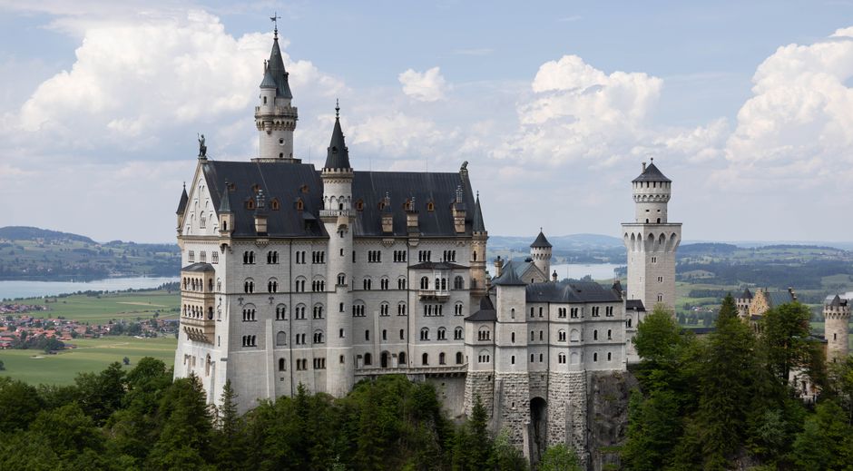 Neuschwanstein Castle, a white medieval fortress with multiple towers against blue sky`