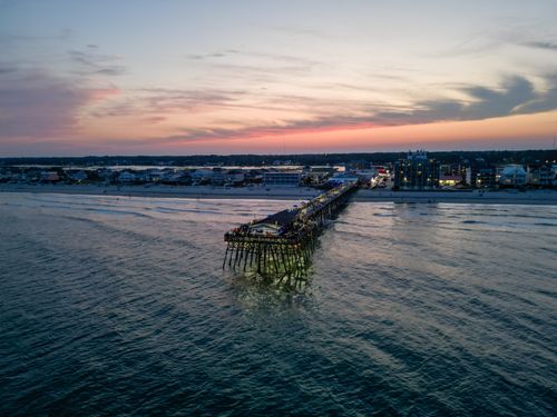 Free A breathtaking aerial shot of a pier extending into the ocean at sunset, with a vibrant sky backdrop. Stock Photo