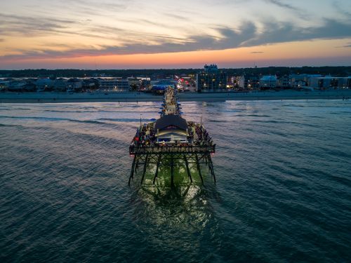 Free A vibrant aerial shot of a crowded pier extending into the sea at twilight with city lights in the background. Stock Photo