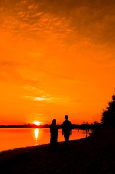 A silhouetted couple walks along a beach at sunset with vibrant orange skies.