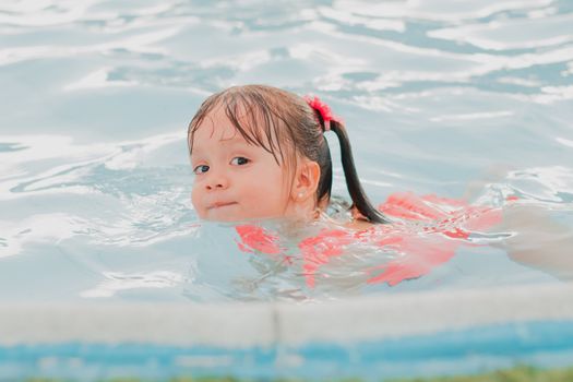 Cute little girl swimming and having fun in a clear pool on a sunny day.