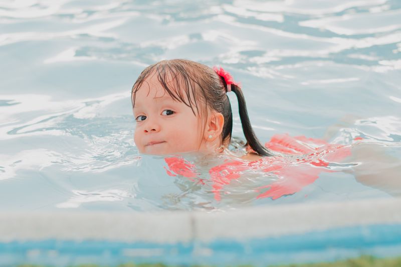 Cute little girl swimming and having fun in a clear pool on a sunny day