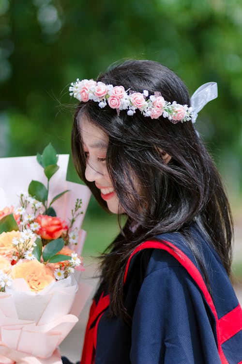 Young Brunette Woman in Graduation Gown and Floral Headband Holding a Bouquet